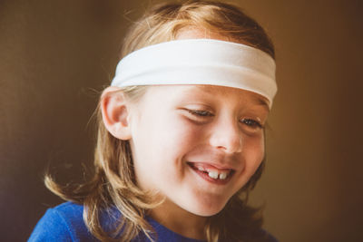 Long haired child with headband smiling and looking downward 