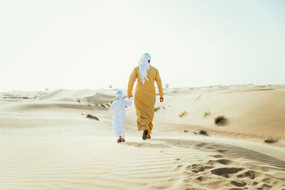 Rear view of man walking on sand dune