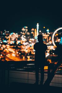 Rear view of silhouette man standing against illuminated city at night