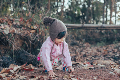 Cute baby girl crouching and playing with leaves during winter