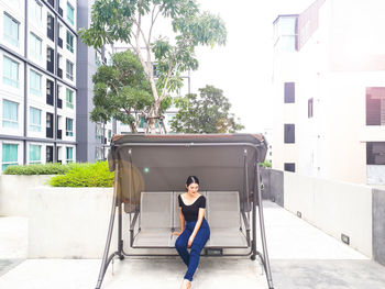 Full length of woman sitting on swing against buildings in city