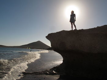 Low angle view of woman standing on cliff against clear sky during sunny day