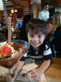 Portrait of cheerful boy having ice cream on table in restaurant