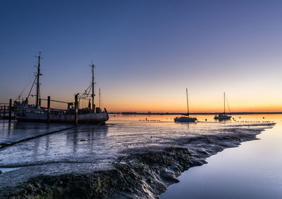 Sailboats moored on sea against clear sky during sunset