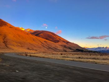 Empty road by mountain against blue sky during sunset