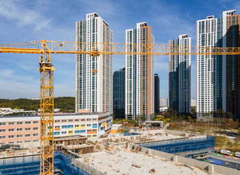 Yellow hoisting crane and a buildings under construction, front view