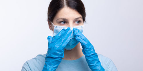 Doctor in mask wearing surgical glove looking away against gray background