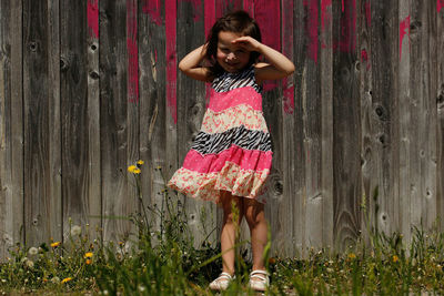 Full length portrait of smiling girl standing in yard against wooden fence