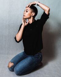 Young woman looking away while kneeling against gray wall