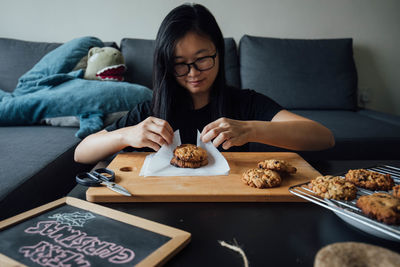 Smiling woman wrapping cookie in paper at home