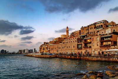 View of buildings at waterfront against cloudy sky