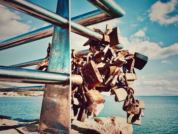 Close-up of padlocks on chain by sea against sky