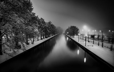 Canal amidst illuminated trees against sky during winter