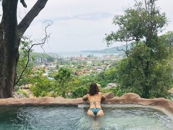 Rear view of shirtless woman against trees and plants against sky