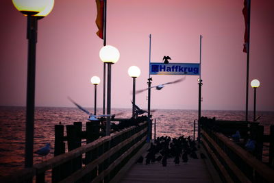 Illuminated street lights on pier by sea against clear sky