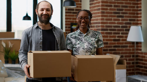 Portrait of smiling couple holding boxes at office