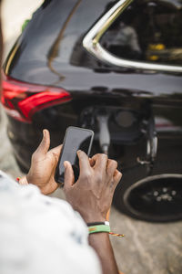 Cropped image of man using smart phone while standing by car on driveway