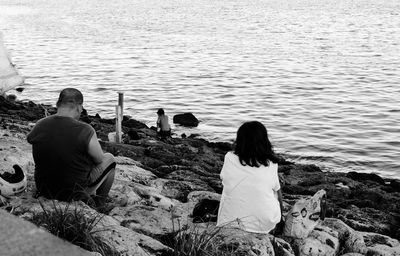 Rear view of people sitting on rock looking at sea