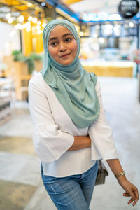 Young woman wearing hijab looking away while standing in restaurant