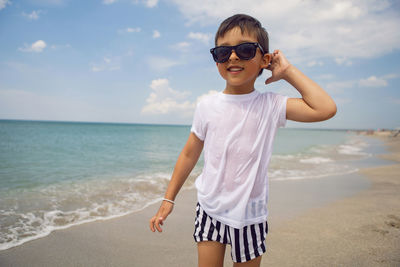 Boy child in striped shorts and a white t-shirt walks on a sandy beach and in sunglasses