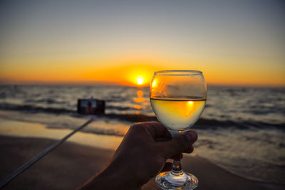 Close-up of hand holding drink at sunset