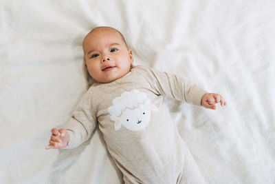 Cute smiling baby boy 4-6 month in beige overall on bed, natural tones