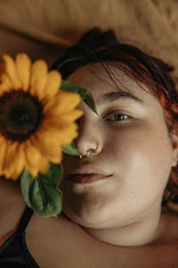 Portrait of young woman wearing nose ring covering eye with sunflower