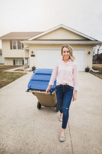 Portrait of woman with garbage bin walking on footpath