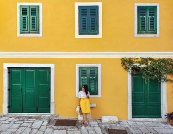 Young woman in summer outfit standing in front of yellow house.