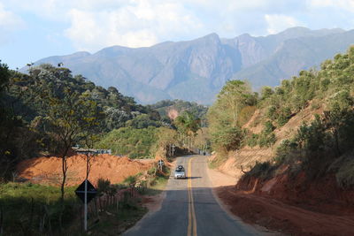 Road amidst trees and mountains against sky