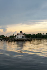 Building by lake against sky during sunset