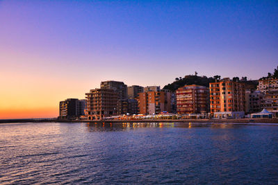 Buildings by sea against clear sky during sunset