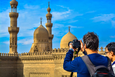 Rear view of people photographing against sky