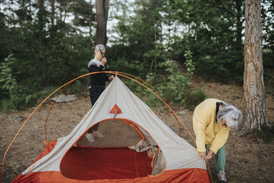 Two senior women setting up tent in forest