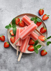 Homemade frozen strawberry ice cream popsicles and fresh strawberries on a concrete background. 