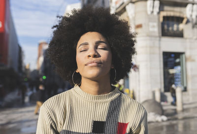 Afro woman with eyes closed standing in city