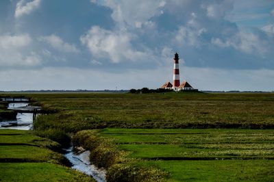 Lighthouse on field by building against sky