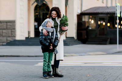 A joyful boy and his young mother are standing in an embrace on the street