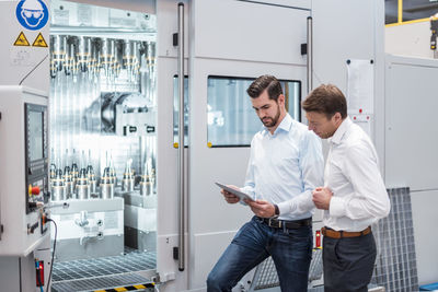 Two men standing at machine in factory looking at tablet