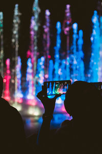 Silhouette woman photographing illuminated fountain at night