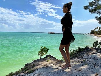 Woman standing on cliff by sea against sky