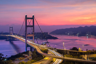 Light trails on bridge over road against sky at sunset