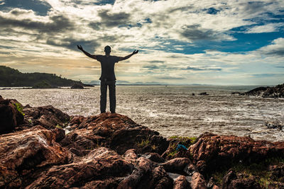 Man standing on rock by sea against sky