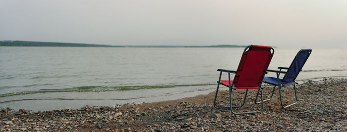 Empty chairs on beach against sky