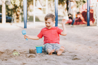 Full length of cute boy playing with sand in playground