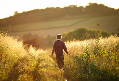 Rear view of boy walking on grassy field