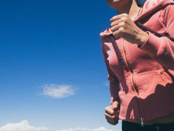 Midsection of woman running against blue sky