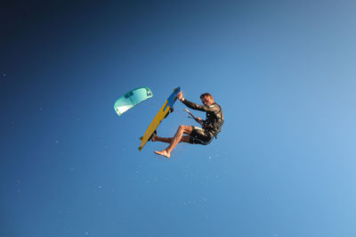A male kiteboarder in flight over the water does a trick in a clear sky with splashes. copy space