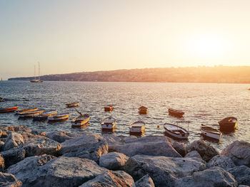 Boats moored in sea against sky at sunset