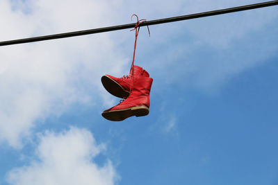 Low angle view of red shoes hanging on cable against sky